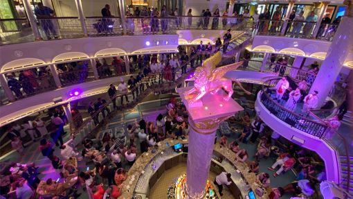 The cruise director speaks to guests in the Carnival Venezia's atrium to recognize the ship's officers.